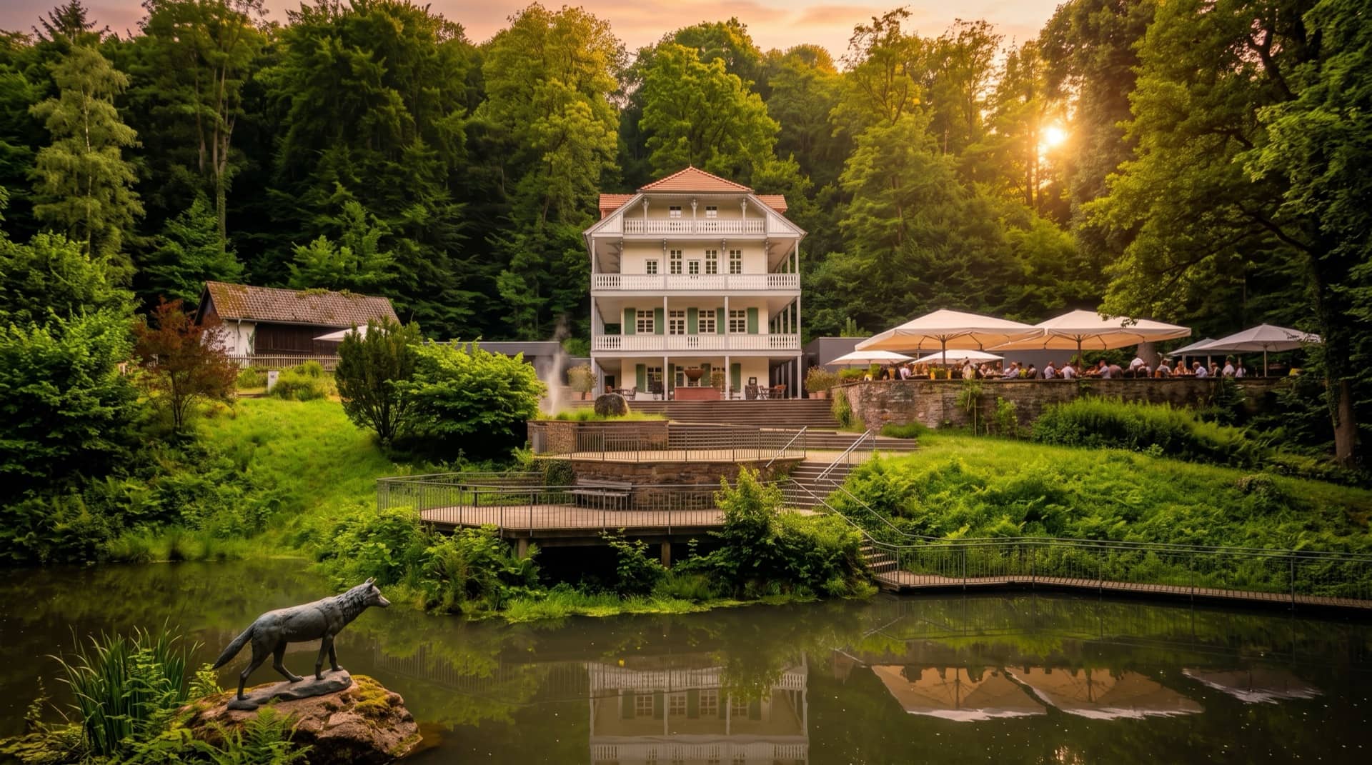 Das Restaurant Wolfsbrunnen in der Abendsonne, vom Teich aus gesehen, mit Terrasse und Gästen